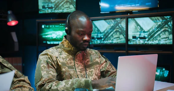 stock image Young African American man dispatcher in headset working on laptop computer in control room.