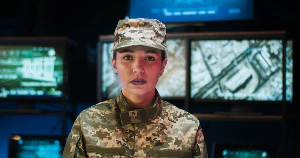 Portrait of beautiful Caucasian female soldier in cap standing in monitoring room and looking straight to camera with smile. Close up of good looking woman army officer smiling in controlling center.