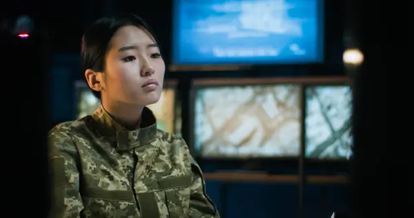 Asian young beautiful woman in camouflage uniform working in military monitoring center at computer screen. Female soldier in army controlling room.