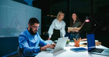 Akşamları dizüstü bilgisayarda çalışan gözlüklü beyaz bir adam. İki güzel bayan iş arkadaşı belgelerini okurken ve gemide yazarken bazı projeler hakkında konuşuyor ve tartışıyorlar..