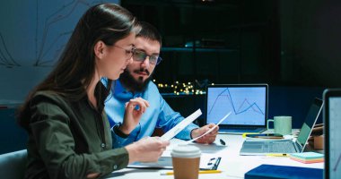 Gece geç saatlerde dizüstü bilgisayarda birlikte çalışan birkaç beyaz erkek ve kadın meslektaşı kadın ofis çalışanının omzunun üzerinden bakın. Akşamları takım çalışması.