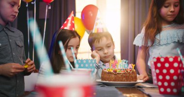 Masaya dayanmış şirin beyaz çocuk doğum günü partisinde arkadaşlarının arasında pastaya sıkılmış görünüyordu. Çocukların doğum günü partisi konsepti.