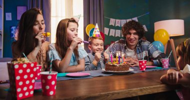 Küçük oğlunun doğum gününü kutlayan neşeli beyaz ailenin portre fotoğrafı. Çocuk pastaya mum üflerken..