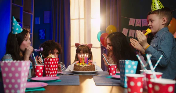 快乐的白人家庭庆祝小女儿的生日 爸爸带着蛋糕 女儿和妈妈吹着蜡烛 图库照片