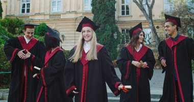 Genç melez ırklar, neşeli kızlar ve erkekler mezuniyet töreninde diploma aldıktan sonra keyifle yürüyen ve eğlenen mezun öğrenciler..