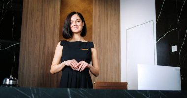 Lüks bir otelde çalışan, kameraya bakıp gülümseyen siyah elbiseli güzel profesyonel resepsiyonistlerin portresi. Müşteri hizmetleri sunan başarılı bir kadın yönetici olarak çalışıyor.