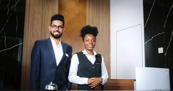 Portrait of elegant hotel staff in uniform. Male and female courteous professionals. Indian and African-American hotel receptionists smiling while looking at camera.