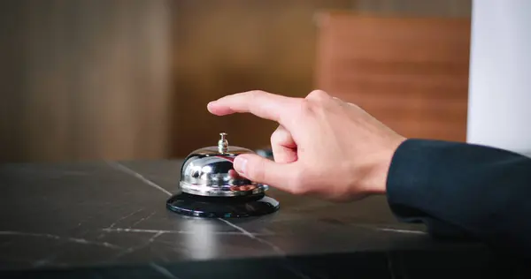 Close-up view of successful businessman ringing bell at reception. Professional receptionist and visitor shaking hands. Elegant guest receiving key card for hotel room. Customer service concept.
