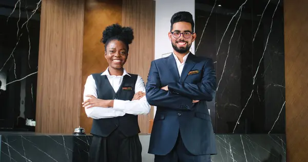 Portrait of team of professional polite and hospitable male and female receptionist standing with crossed arm looking at camera and smiling. Attractive happy workers of hotel.