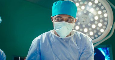 Afrikalı Amerikalı doktor kapat. Özel şapkalı ve koruyucu maskeli bir doktor. Ameliyat odasının arka planındaki doktor. Doktor asistana makas verir. Sağlık çalışanları ameliyat yapıyor..