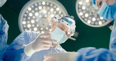 Aşağıdan ateş et. Cerrahi müdahale sırasında yakın çekim tıbbi çalışanlar. Kadın stajyer doktor asistanı. Dürbünlü doktor ameliyat yapıyor. Ameliyathanede sağlık çalışanları var..