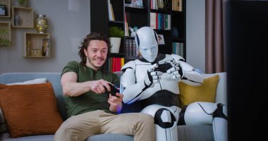 Robot gibi gelecekçi bir insan ve TV karşısında koltukta otururken konsolda oyun oynayan mutlu bir genç adam. Yapay zeka ve boş zaman kavramı.