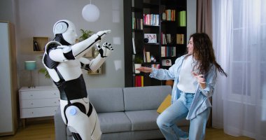 Parlak oturma odasında sibernetik robotla neşe içinde dans eden çekici bayan. Cyborg gibi zeki bir insan çekici beyaz bir kadınla eğleniyor..