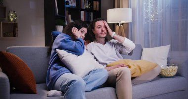 Kadın oturma odasında patlamış mısır yiyip televizyon seyrederken, odaklanmış adam uzaktan modern dizüstü bilgisayarla çalışıyor. Neşeli çift akşamları evde birlikte vakit geçiriyorlar..