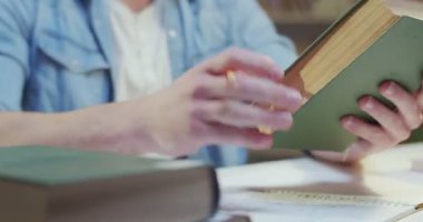 Yakışıklı beyaz bir erkek öğrencinin eski bir kitabı eline alıp önemli bilgilere dikkat çekmesi. Kütüphanede ders kitaplarıyla çalışmak. Eğitim kavramı.