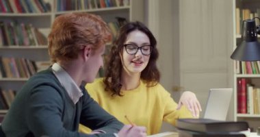 Kafkasyalı bir çift öğrenci kütüphanede konuşuyor ve birlikte çalışıyorlar. Erkek notlar yazıp önemli bilgilere dikkat çekiyor, kadın açıklama yapıyor. Biblioeca konsepti. Özel ders.