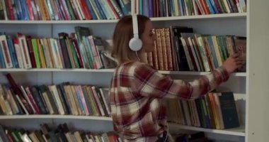 Kafkasyalı kulaklıklı güzel bir kız öğrenci kütüphanede ders kitabını seçiyor ve çalışmak için masaya oturuyor. Sarışın kadın İncil 'deki raftan kitap alıyor ve okuyor..