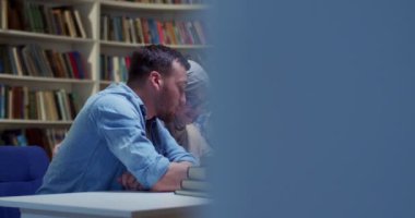 Karışık ırklar genç erkekler ve bayan arkadaşlar kütüphanede masada oturmuş neşeyle konuşuyor ve öğreniyorlar. Erkekler ve kadınlar, bibliyotheca 'daki proje üzerine beyin fırtınası yapıyorlar..