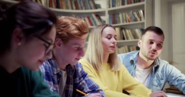 Beyaz, genç, erkek ve kız öğrencilerden oluşan bir takım kütüphanede ders çalışmak hakkında konuşuyor ve tartışıyorlar. Bibliyotheca 'da sohbet eden neşeli insanlar. birlikte öğrenme kavramı.