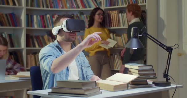 在Vr耳机中的白种人男生坐在图书馆空间中 双手在空中打滚和移动 并具有虚拟现实的经验 代谢研究 虚拟概念研究 — 图库视频影像