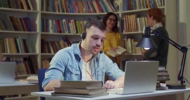 在笔记本电脑学习 视频聊天和记笔记的白人年轻男生 在图书馆工作视频呼叫并在书目中写下信息 视频聊天 — 图库视频影像