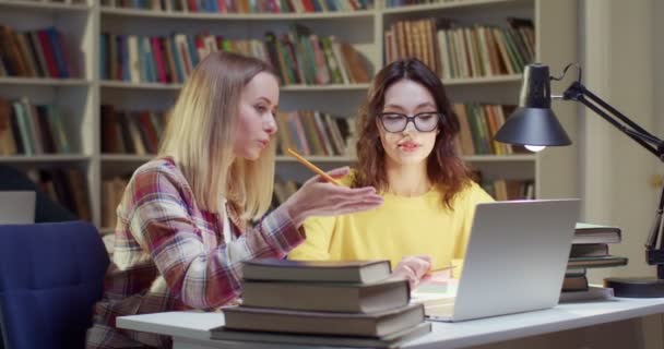 两名在笔记本电脑上学习的白人年轻女生一起在图书馆学习 Biblitheca概念 向朋友解释 并准备一起考试 朋友在学习 妇女讲话和学习 — 图库视频影像