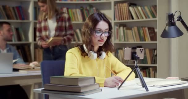Female Headset Glasses Talking Writing Videochatting Smartphone Library Woman Speaking — Stock Video