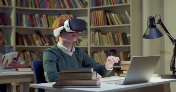 在Vr耳机中的白人年轻男生坐在图书馆空间中 双手在空中打滚和移动 并具有虚拟现实的经验 代谢研究 虚拟概念研究 — 图库视频影像