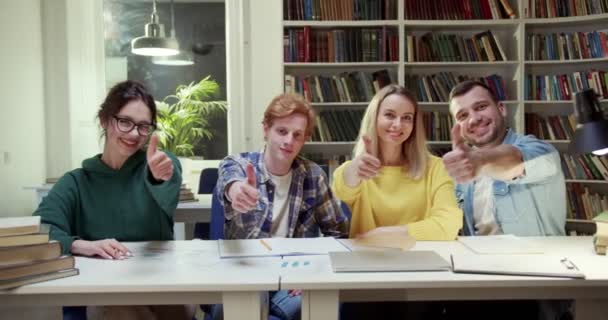 照片中 一群年轻的白人快乐的男生和女生坐在图书馆的餐桌前 把大拇指放到相机前 男人和女人在学习的时候都很快乐 也很开心 — 图库视频影像