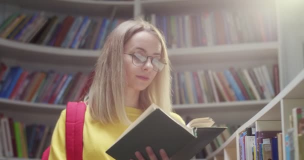 接近年轻的白种人漂亮的金发女学生 戴着眼镜站在图书馆看书 聪明的女人读参考书 教育你自己学习概念 — 图库视频影像