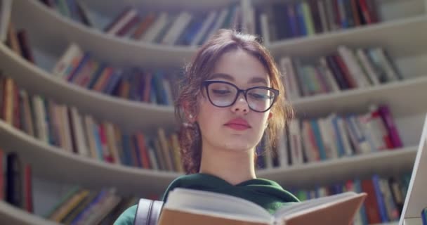 接近白种人漂亮的女学生 戴着眼镜翻页 在图书馆里搜寻信息 文学概念 书架上有教科书的妇女 — 图库视频影像
