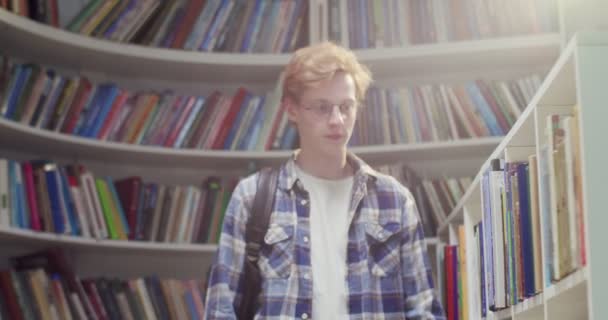 Молодой Рыжеволосый Белый Студент Рюкзаком Гуляющий Библиотеке Выбирающий Учебник Чтения — стоковое видео