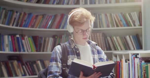Estudante Cabelos Vermelhos Caucasiano Óculos Fones Ouvido Lançando Páginas Lendo — Vídeo de Stock