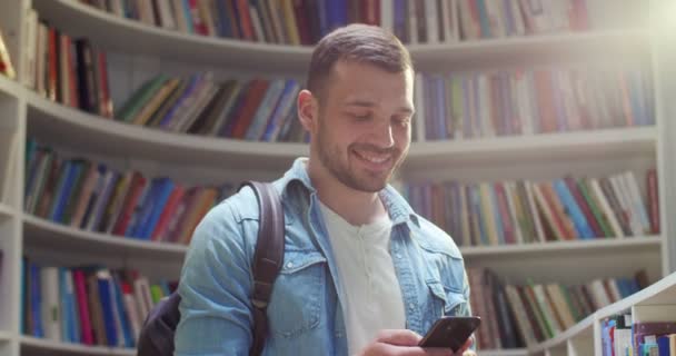 Молодой Кавказский Студент Рюкзаком Болтает Смартфоне Отправляет Сообщения Библиотеку Парень — стоковое видео