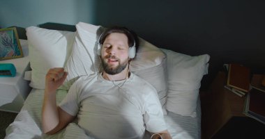 Rüya gibi çekici genç adam yatakta uzanıyor, gülümsüyor ve kulaklıkla müzik dinliyor. Neşeli hissediyorum, ritim içinde hareket ediyorum, şarkı söylüyorum..