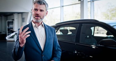 Kameraya araba anahtarlarıyla övünen, dans eden neşeli beyaz adamın yakın plan portresi. Galeride indirimli satış yapan mutlu bir satıcı. Araba bayiliği, araba işi..