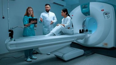Beyaz önlüklü doktor MRI görüntüsünü inceliyor. Hasta MRI kapsülünde yatıyor. MRI dolabı. Modern ekipmanlar özel klinikte. Hemşire üniforması tablet taşıyor. MRI testi. Kısırlık prosedürü.