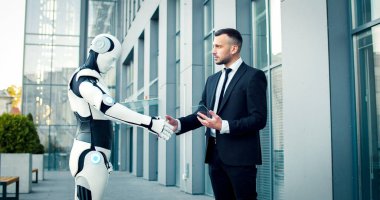 Müdür, iş merkezinin yanında duran robotla el sıkışıyor. Erkek, yapay zeka makinesine, adamın elindeki cihazla yardım ettiği için teşekkürler..