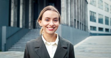 Memnun bayan yönetici iş merkezinin yanında duruyor. Beyaz kadın neşeyle gülümsüyor. Mutluluk girişimcilerin yüzüne yansıyor.