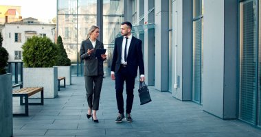 İki çalışan iş merkezinde yürümekten bahsediyor. İş kıyafeti giyen beyazlar iş meselelerini tartıştılar.