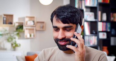 Tatmin olmuş Arap erkek portresi evde otururken telefonda konuşuyor. Sakallı adam gülümsüyor eski bir dostla keyifli bir konuşma yapıyor..