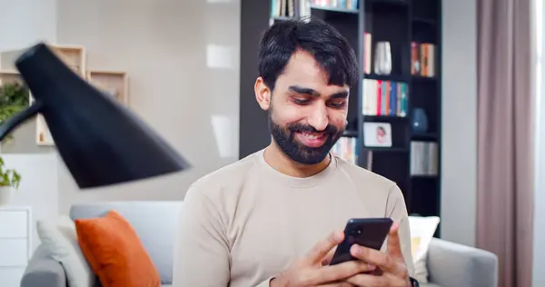 stock image Close up portrait of Arabian male holds phone in hands. Bearded face man smiles chatting online with friend on device.