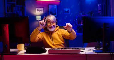 Kafasında kulaklık olan mutlu, beyaz erkek portresi masada farklı aletlerle oturuyor. Yakışıklı sakallı adam LED ışıklı odada müzik dinlemeyi seviyor..