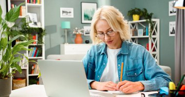 Kafkasyalı genç bir kadının yakın plan portresi masada dizüstü bilgisayarla oturup notlar alıyor. Güzel bir kadın memleketinde okuyor..
