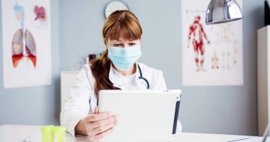 Kafkas kadın doktor portresi boynundaki steteskopla tıbbi maske takıyor ve elinde tablet tutuyor. Özel kıyafetler giyen güzel bir kadın hastanede alet kullanıyor..
