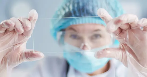 stock image Close up portrait of Caucasian female doctor wearing specialized clothes holds glass in hands. Woman researches new virus in local hospital.