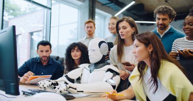 Multi-ethnic group of smart engineers looking at their robot entering text. Checking if program or software operates correctly. Woman next to automated gadget commanding by voice activation. clipart