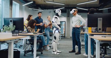 Çok ırklı bir grup araştırmacı yeni bir oluşumu test ediyor. VR kulaklık takan yetişkin bir erkek. Sanal gerçeklik gözlükleriyle insansı robotu çalıştırmaya çalışıyorum. Başarılı bir test. Herkes alkışlıyor..