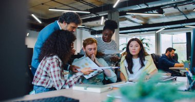 Kamera, beyaz bir erkeğin sandalyede oturduğunu ve yorgun göründüğünü gösteriyor. Çevresindeki meslektaşları verilerle grafikler gösteriyor ve bir şey hakkında haykırıyorlar. İş sorunları. Zor bir gündü. Negatif ortam.