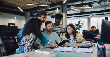 Çoklu etnik gruptan iş arkadaşları kodlarında ya da evraklarında hata arıyorlar. Monitörün önünde oturuyor. İçinde veri olan defterler tutuluyor. Çözüm arıyorum. Arka planda çalışan diğer insanlar.